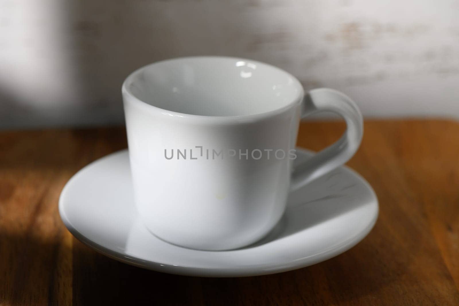 A white coffee cup on a clean saucer glows in the soft morning sunlight, creating a serene scene.