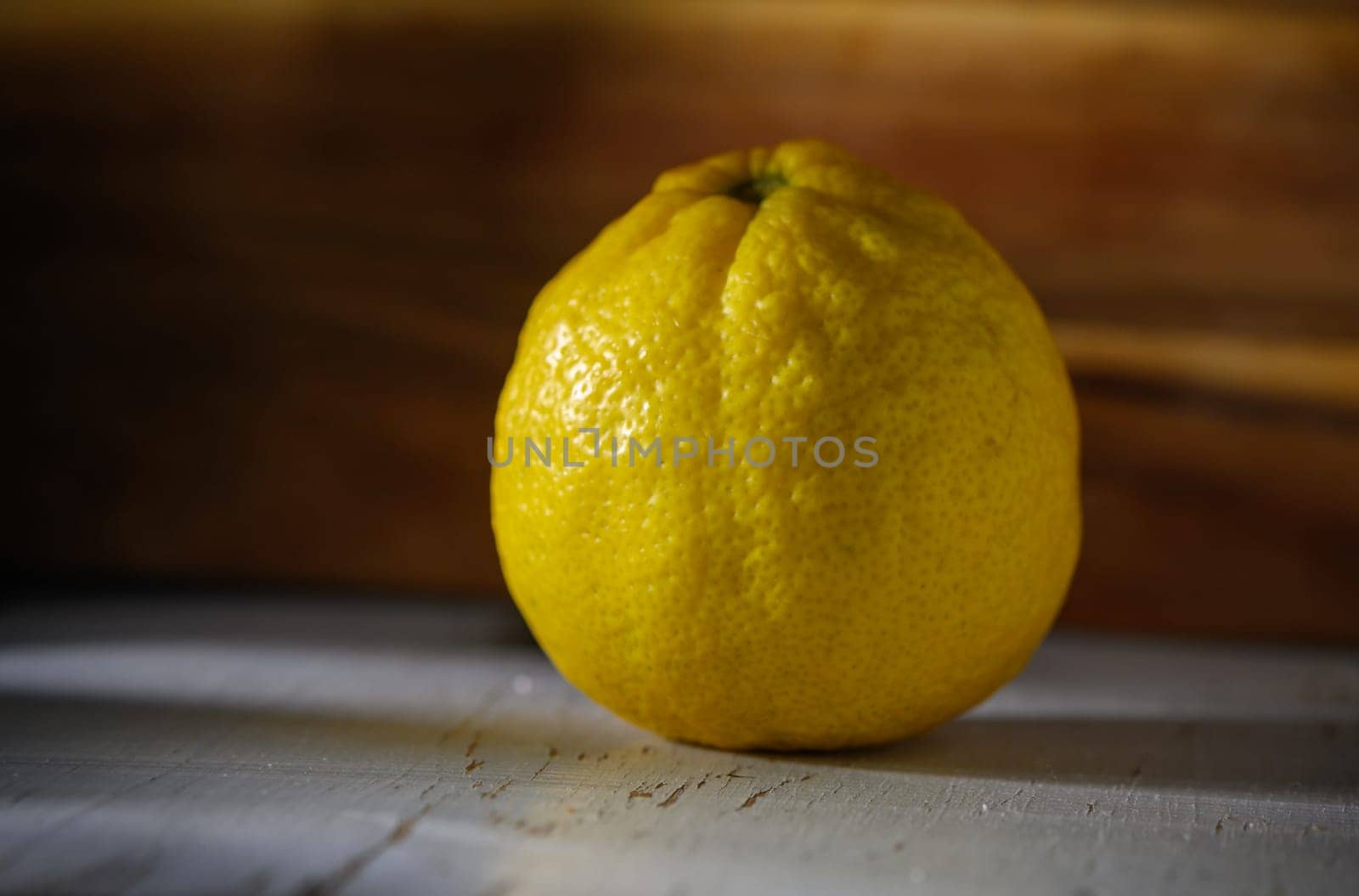 Bright yellow lemon sits alone on a weathered table, illuminated by warm sunlight filtering through nearby windows.