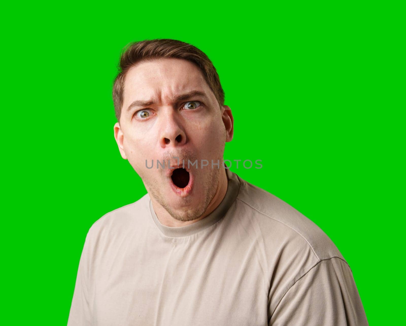 A surprised man stands in front of a bright green screen, expressing shock with his mouth open in studio