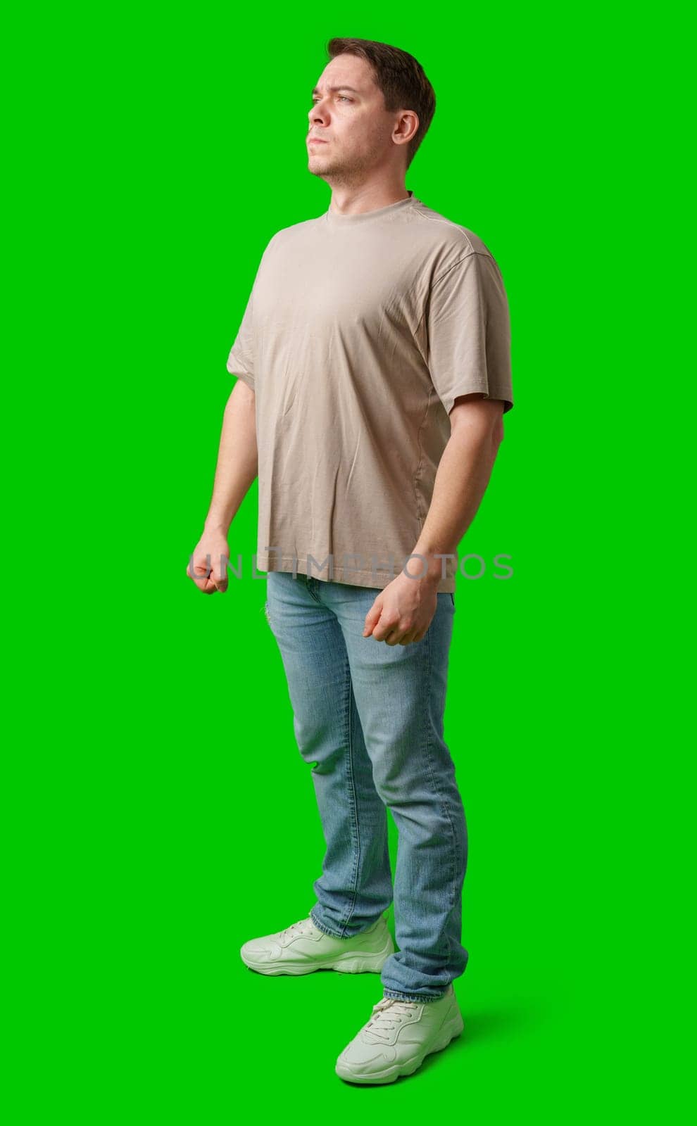 Young man stands confidently in a plain beige t-shirt and jeans against a bright green background in studio