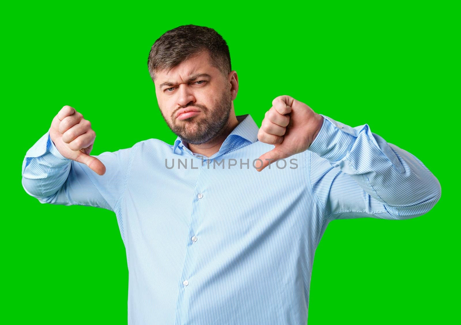 Man expressing disapproval with thumbs down gesture against a bright green background in studio