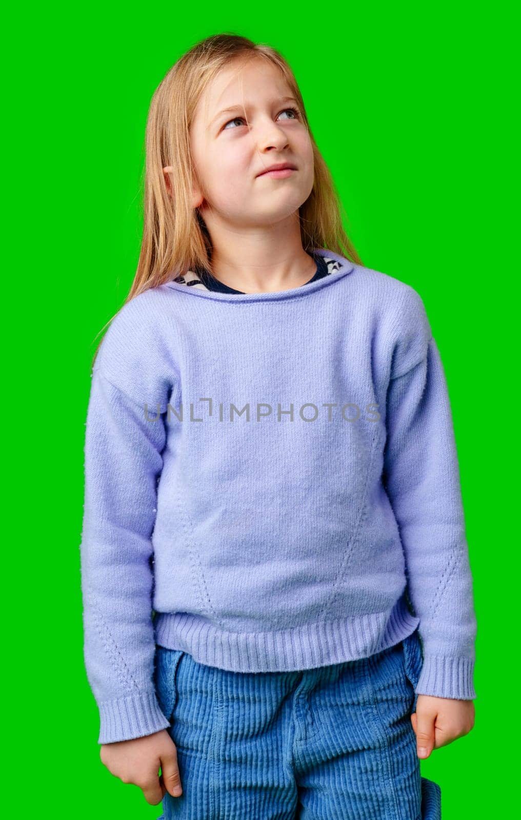 A young child in a light purple sweater gazes against a vibrant green background while deep in thought