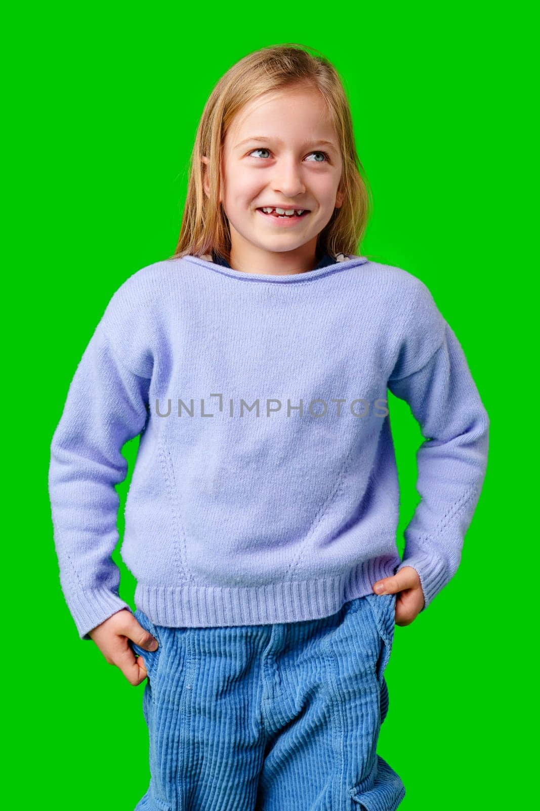 Child wearing a blue sweater and light blue pants stands confidently in front of a green background in a studio