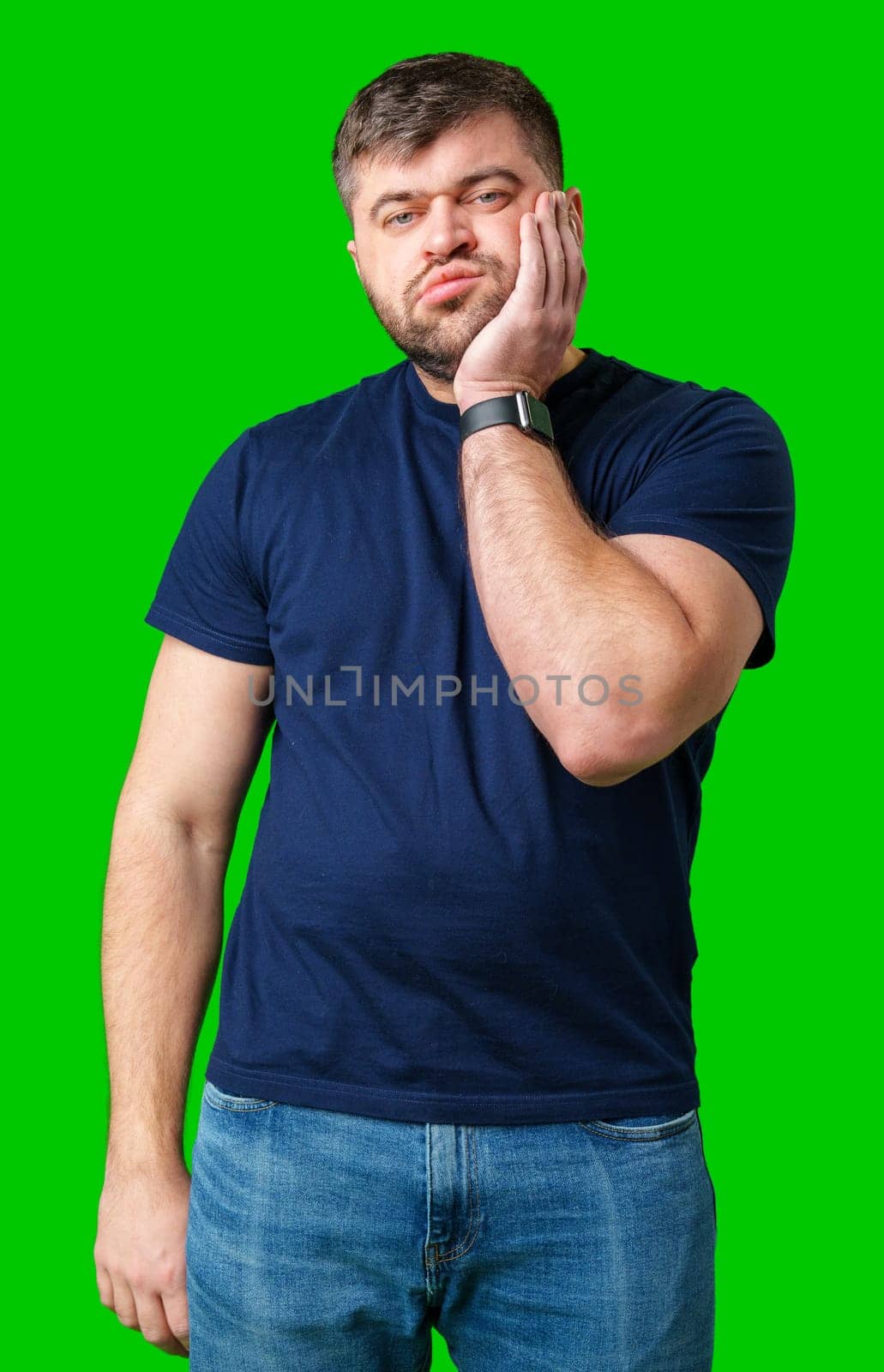 Young man with a contemplative expression leaning against green backdrop while resting his head on his hand in studio