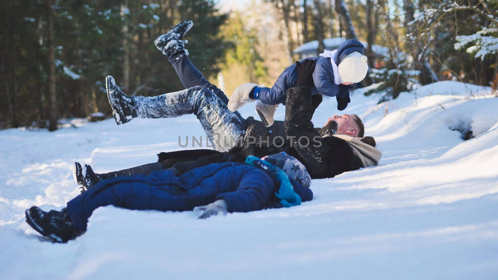 Happy family enjoying quality time together while playing in the snow with their baby, surrounded by serene trees in a winter forest