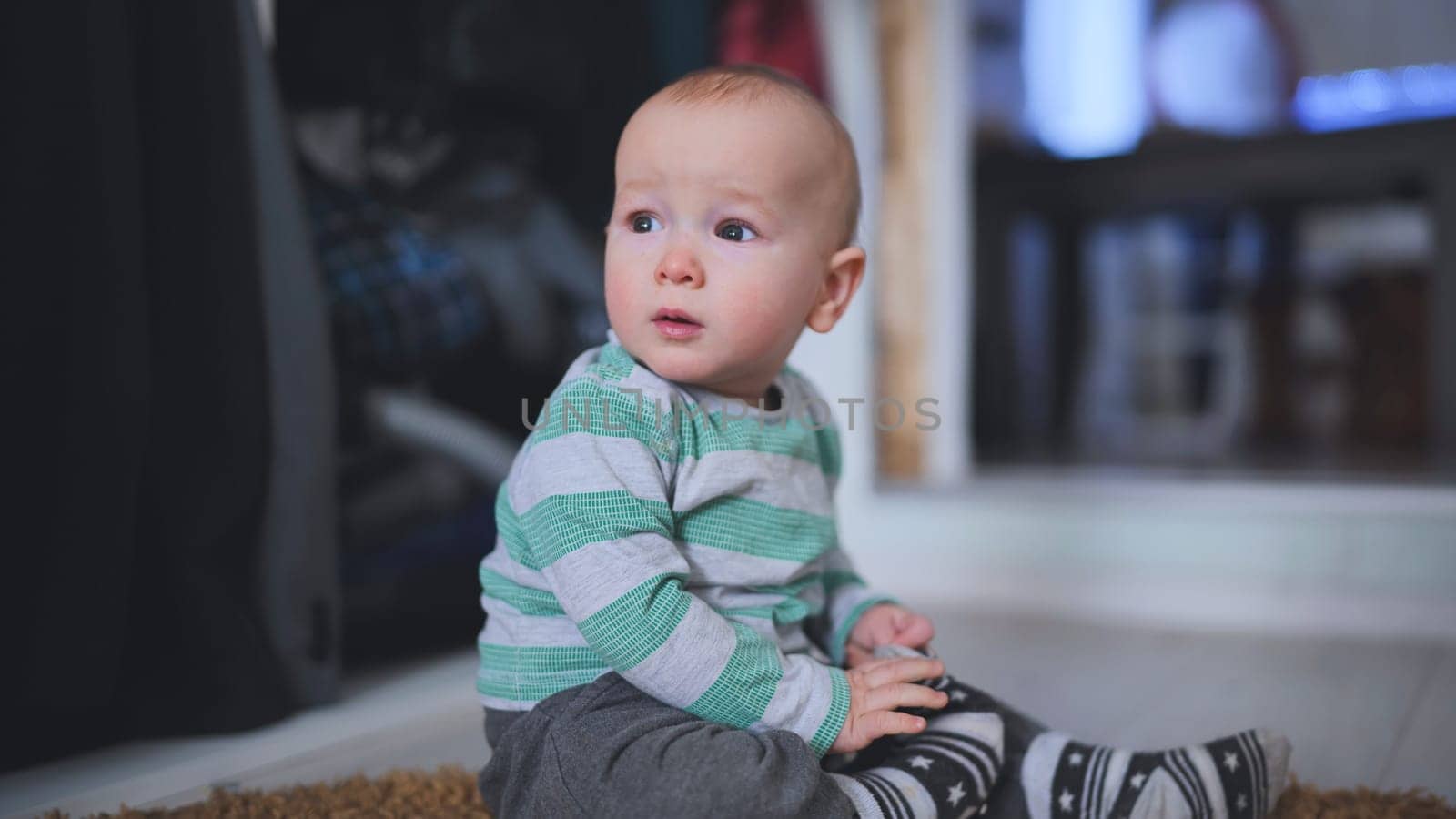 Baby boy sitting on the floor, playing with his feet and looking away from the camera, radiating innocence and curiosity in a cozy home setting