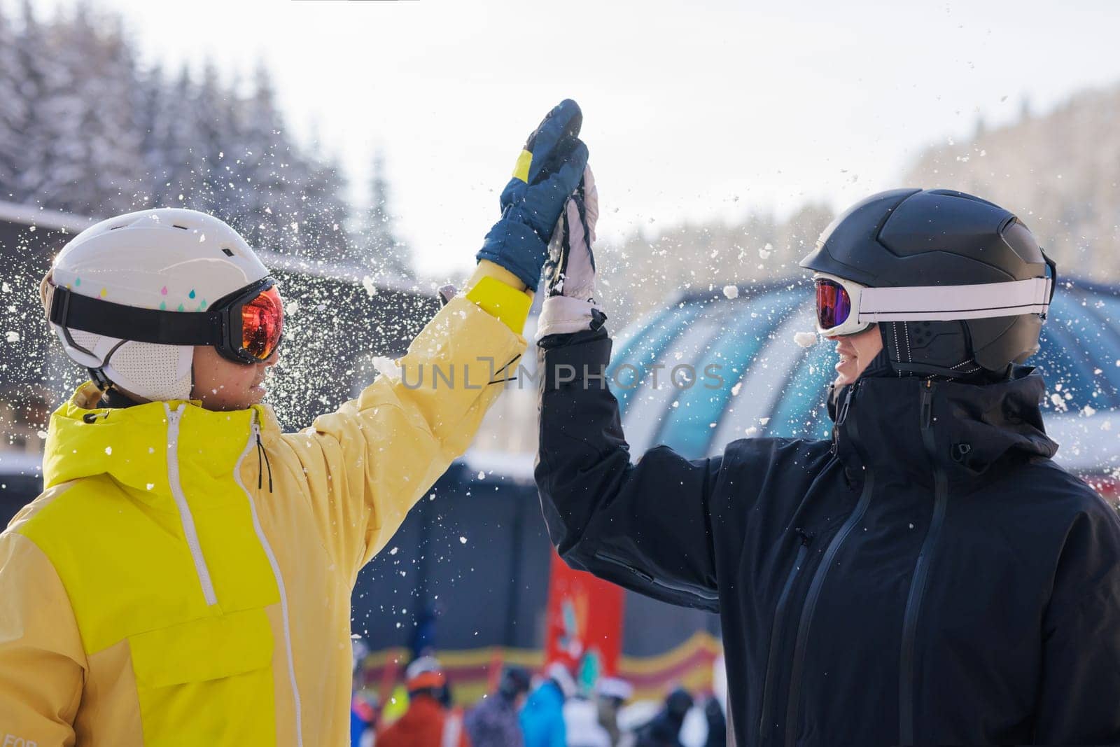 Two skiers in colorful ski gear smiling and slapping each other on the palm and having fun with snow. Ski resort concept,