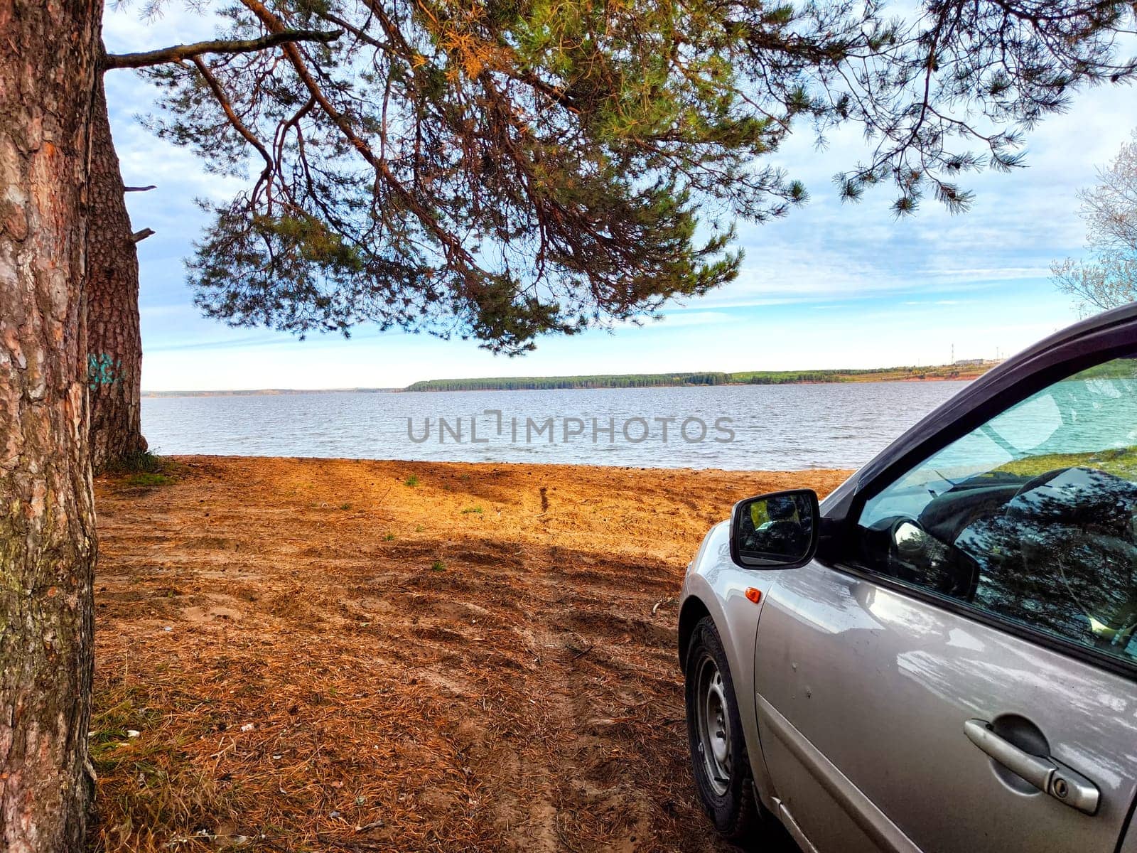A parked car sits by a calm lake surrounded by trees, showcasing a peaceful nature landscape during daytime.