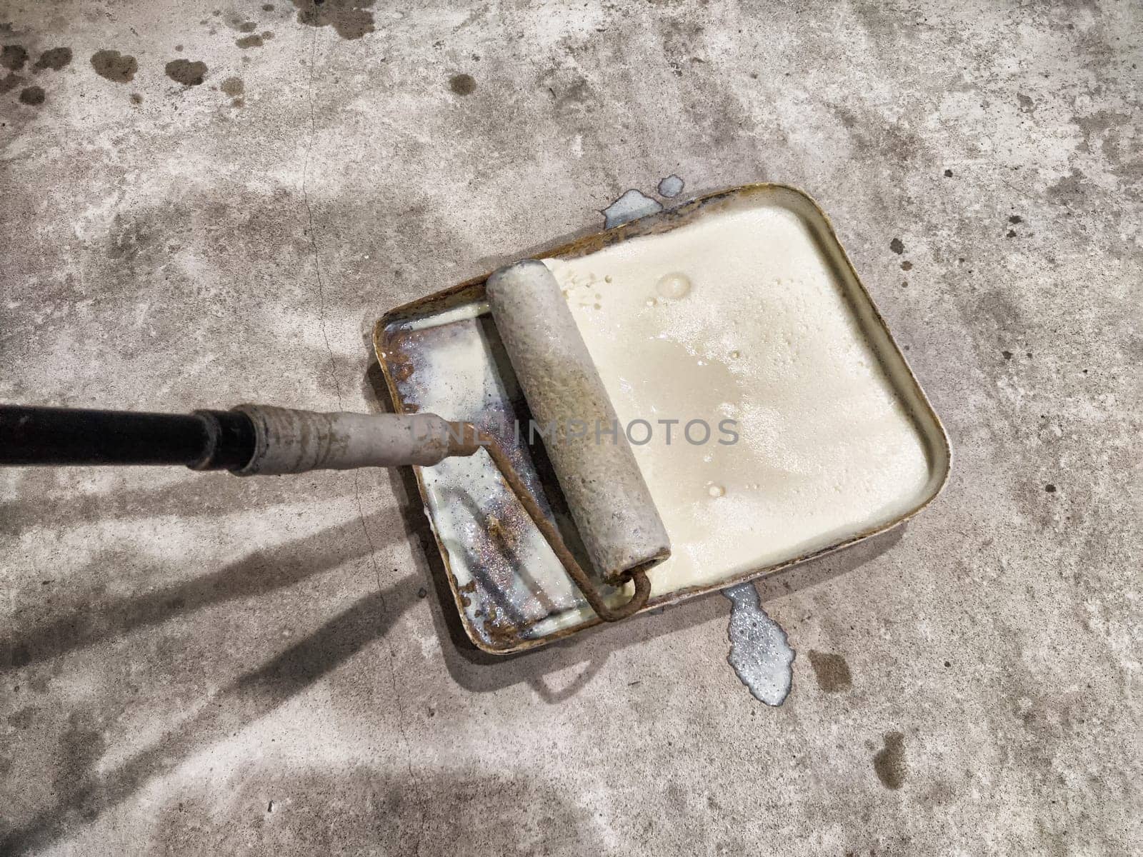 A worker applies primer using a roller on the floor to prepare it for laying tiles in a room undergoing renovation.