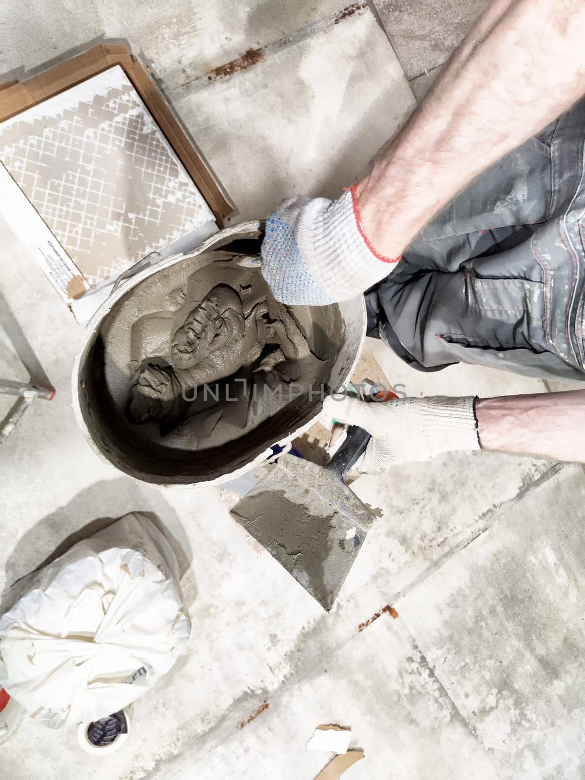 Worker is mixing concrete for indoor tile repair and installation on the floor, surrounded by tools and materials.