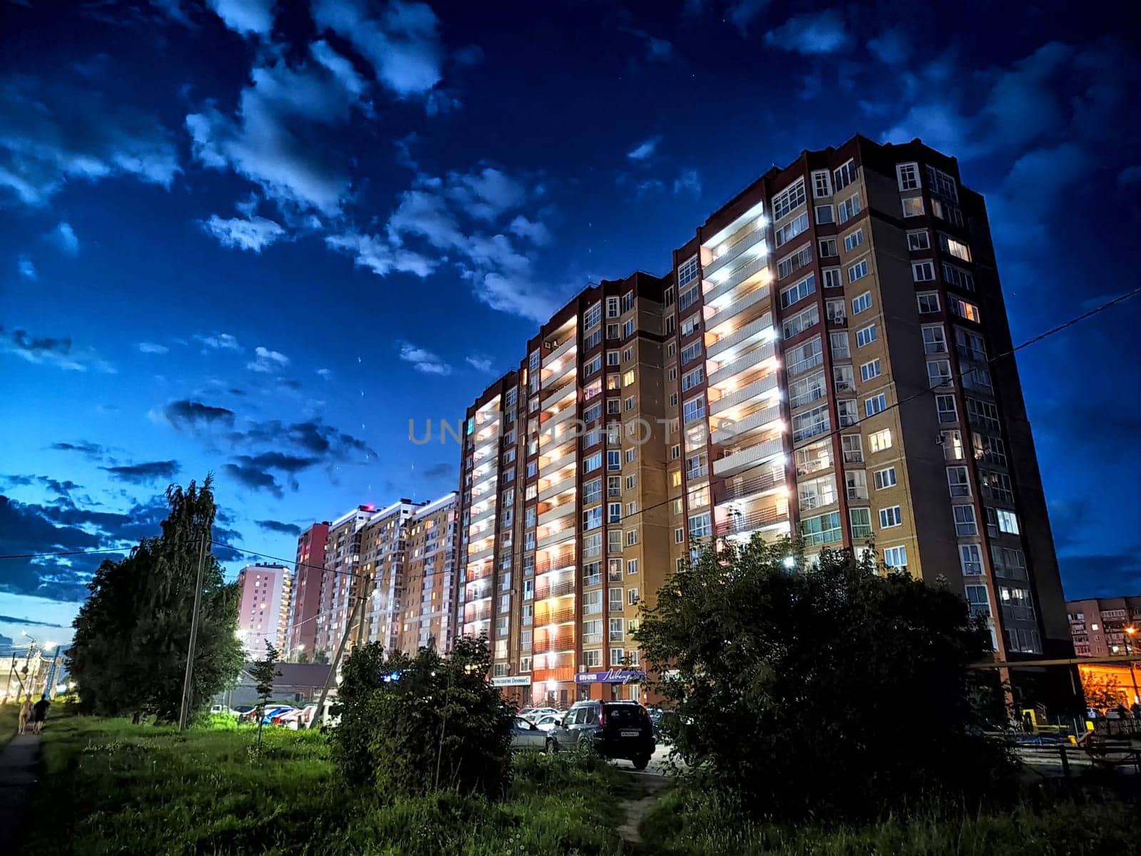 Kirov, Russia - August 11, 2023 - Brightly lit apartment buildings stand tall at night, showcasing warm lights amidst a darkening sky with clouds.