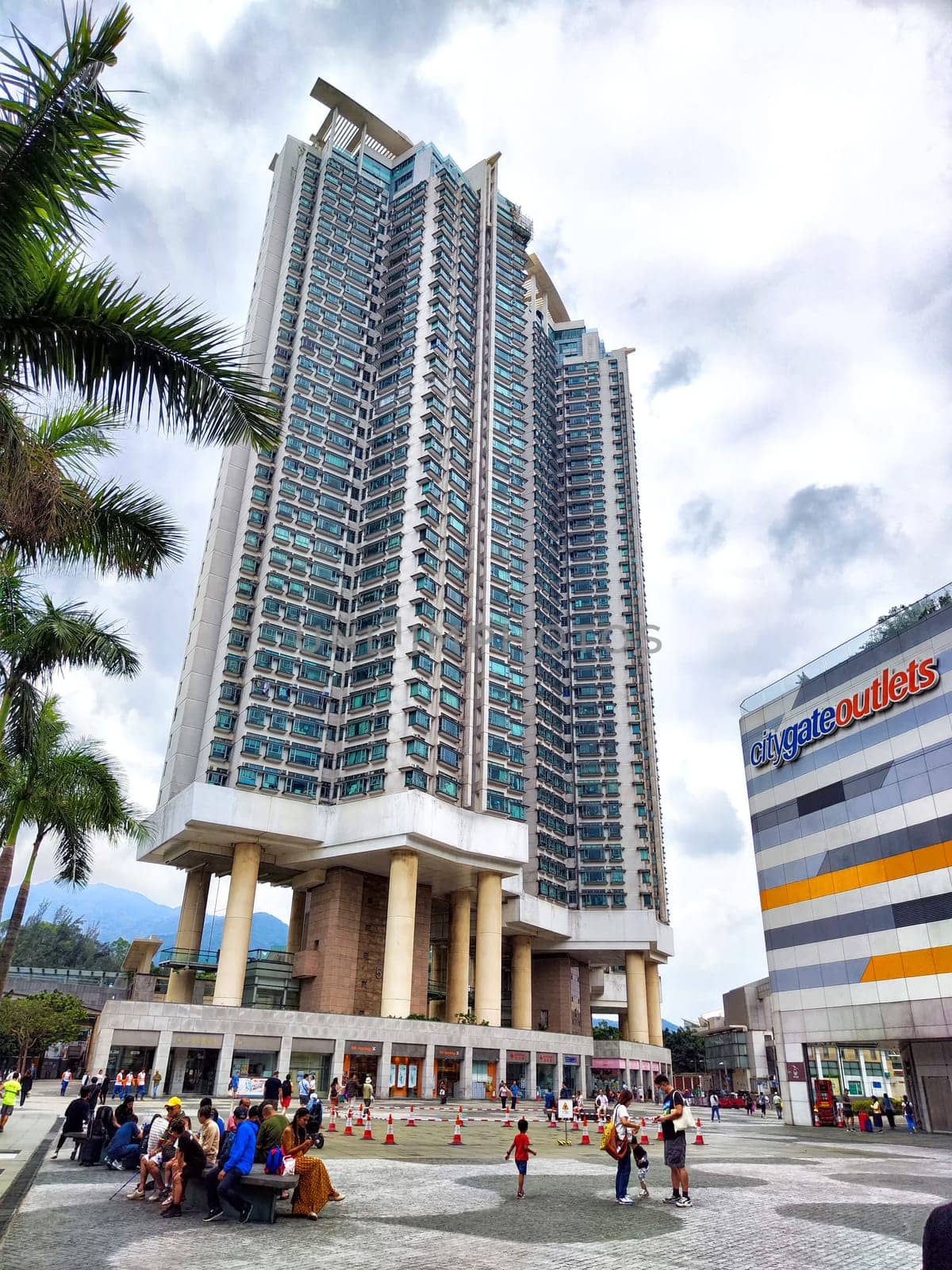 Hong Kong, China - April 08, 2024 - Busy crowds gather at the base of a striking skyscraper as modern architecture rises against the cloudy sky in Hong Kong.