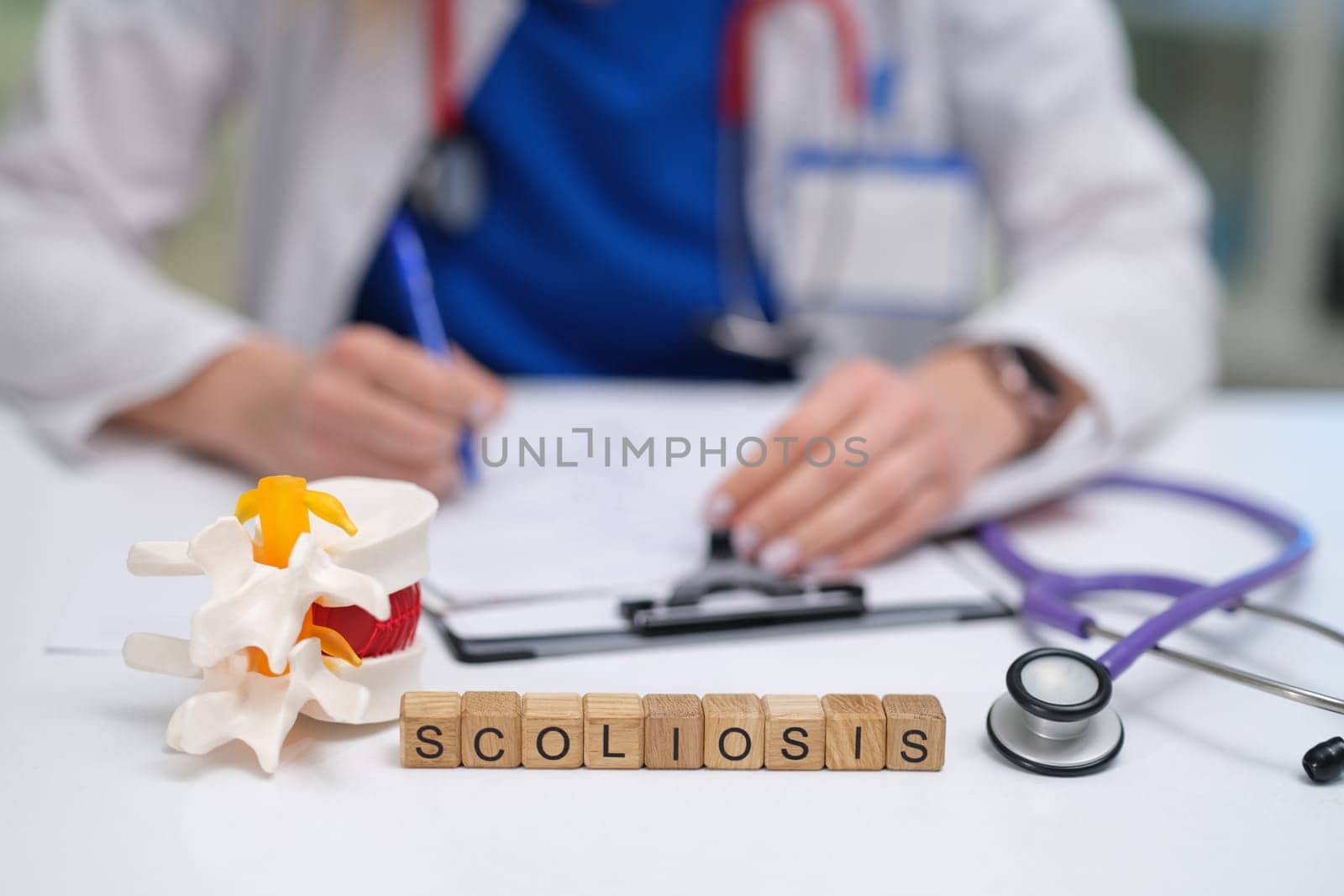 During a consultation, a doctor performs an examination of scoliosis using a detailed spine model and notes findings