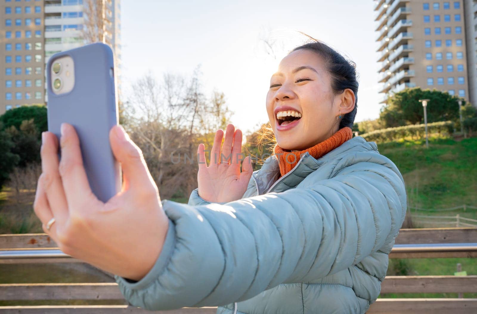 A joyful woman is engaging in a lively video call, wearing a bright smile, set against a sunny and vibrant background