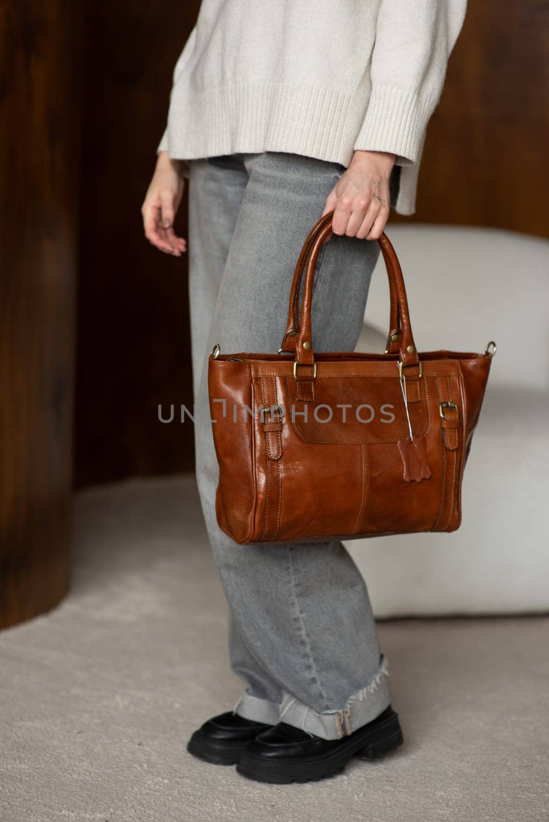 beautiful girl in gray pants and beige sweater posing with a small brown leather bag.