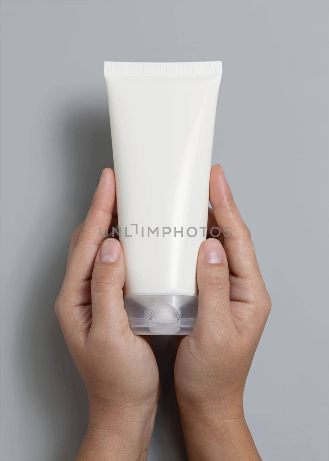 Female hands holding white squeeze cream tube against grey top view, cosmetic package mockup, copy space. Skincare beauty product