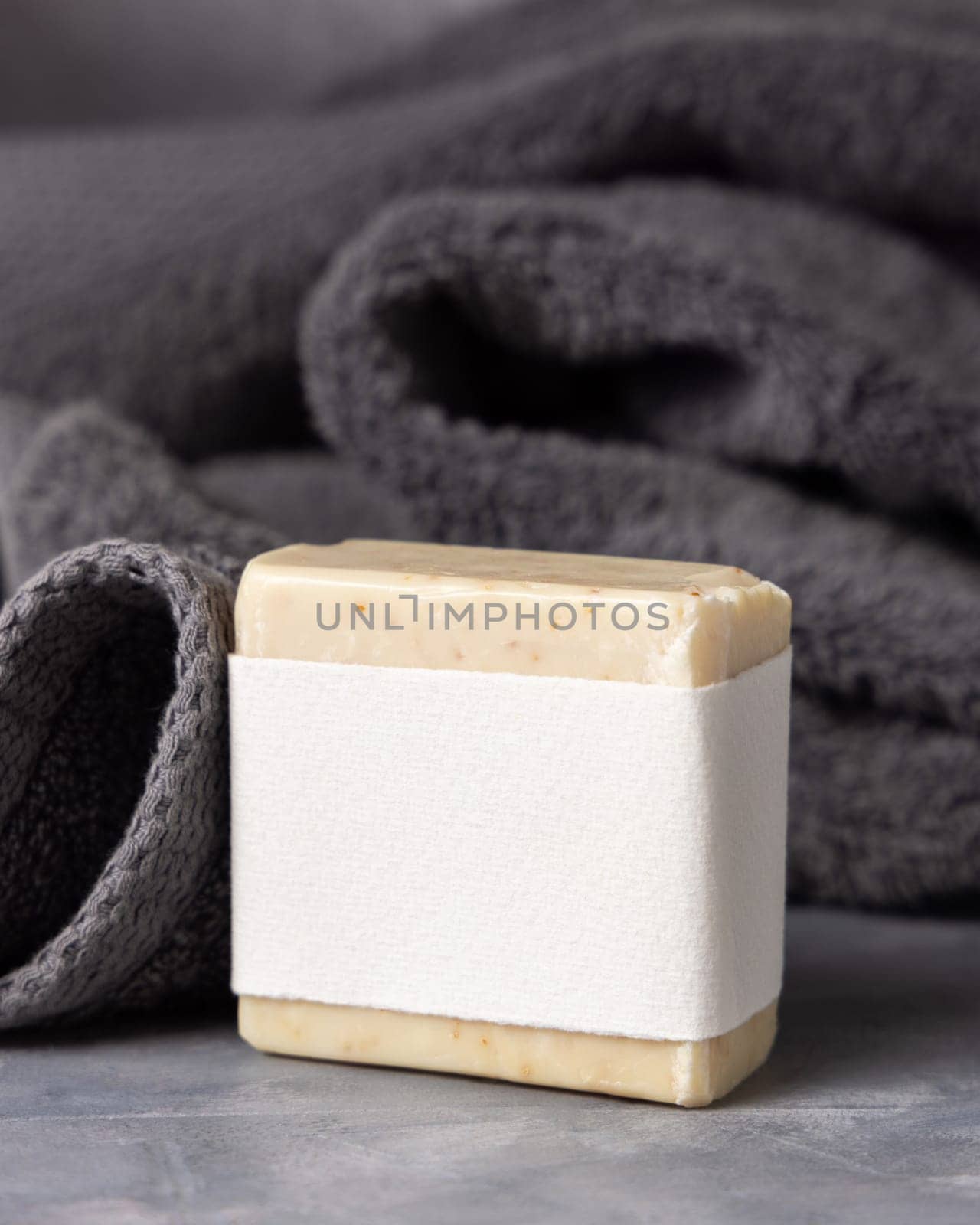 Beige handmade soap bar with blank label near dark grey folded towel closeup, packaging mockup, copy space. Natural herbal hygiene soap for daily cleansing and skincare