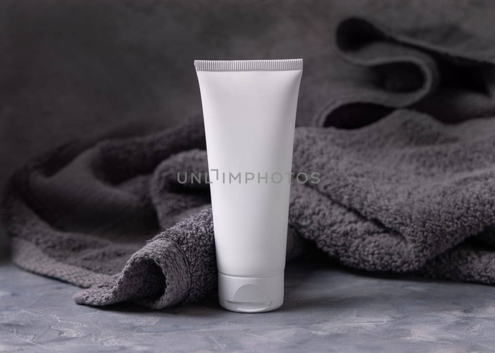 White blank cosmetic squeeze cream tube on dark grey towel in bathroom closeup, brand packaging mockup, copy space. Natural handmade cosmetic product for facecare and spa procedures