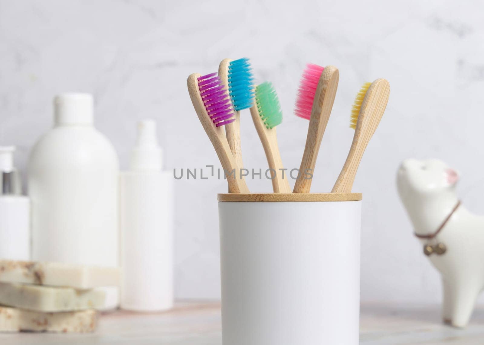 Eco-friendly colorful bamboo toothbrushes in holder cup in a white in bathroom against natural cosmetics, mockup. Zero waste concept, personal care and hygiene products