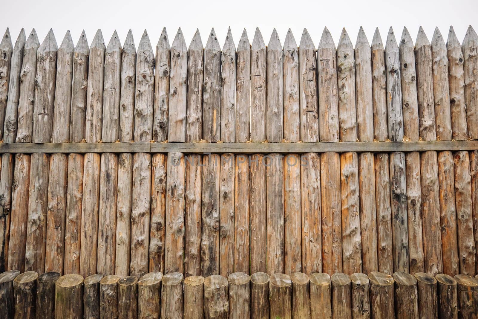 Weathered wooden palisade standing tall, revealing defensive structural integrity of ancient fortification methods with sharp pointed vertical logs