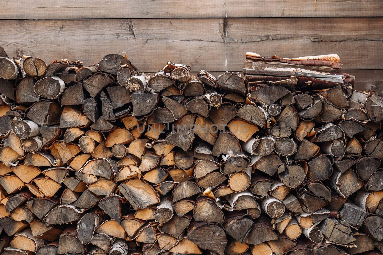 Firewood logs stacked and drying near a wooden wall in a rural area of russia, creating a rustic and traditional scene