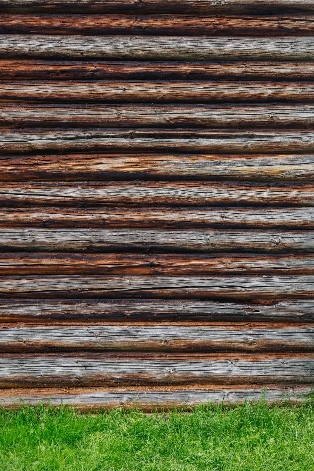 Weathered wooden logs forming a rustic wall, showcasing traditional russian architecture with vibrant green grass at the base