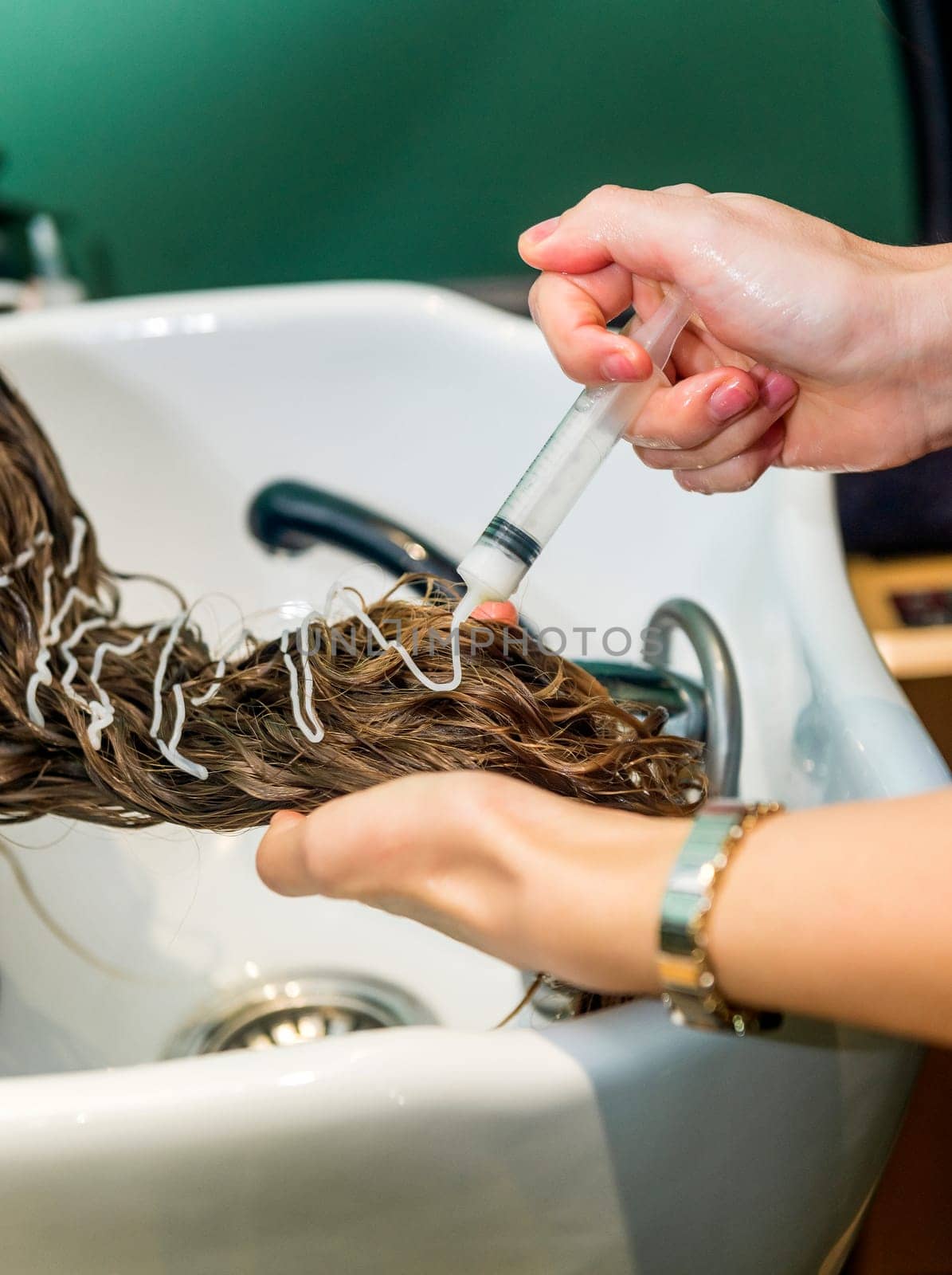 client's hair is treated with hair cream. hairdresser applies white solution from syringe to client's hair. hair strengthening procedure. close-up of client's head, keratin application procedure
