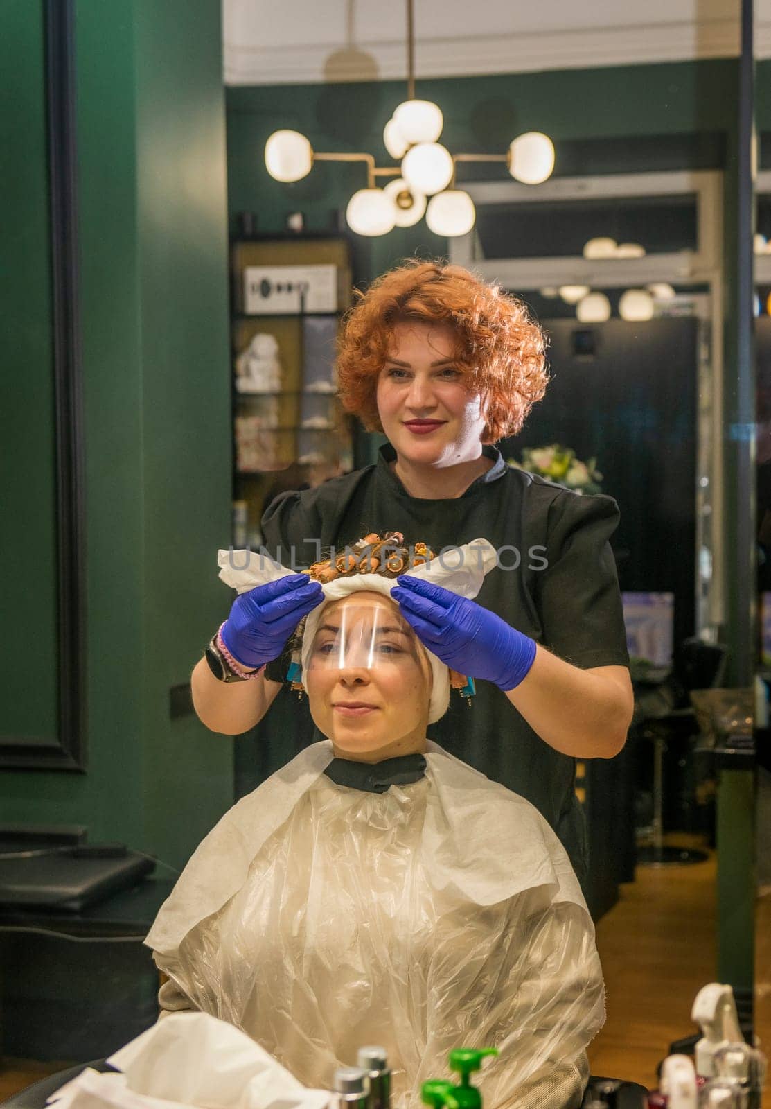 A young girl is getting her hair curled with curlers by a hairdresser. The client is sitting in a chair in a beauty salon. Her hair is being styled for the hair curling procedure