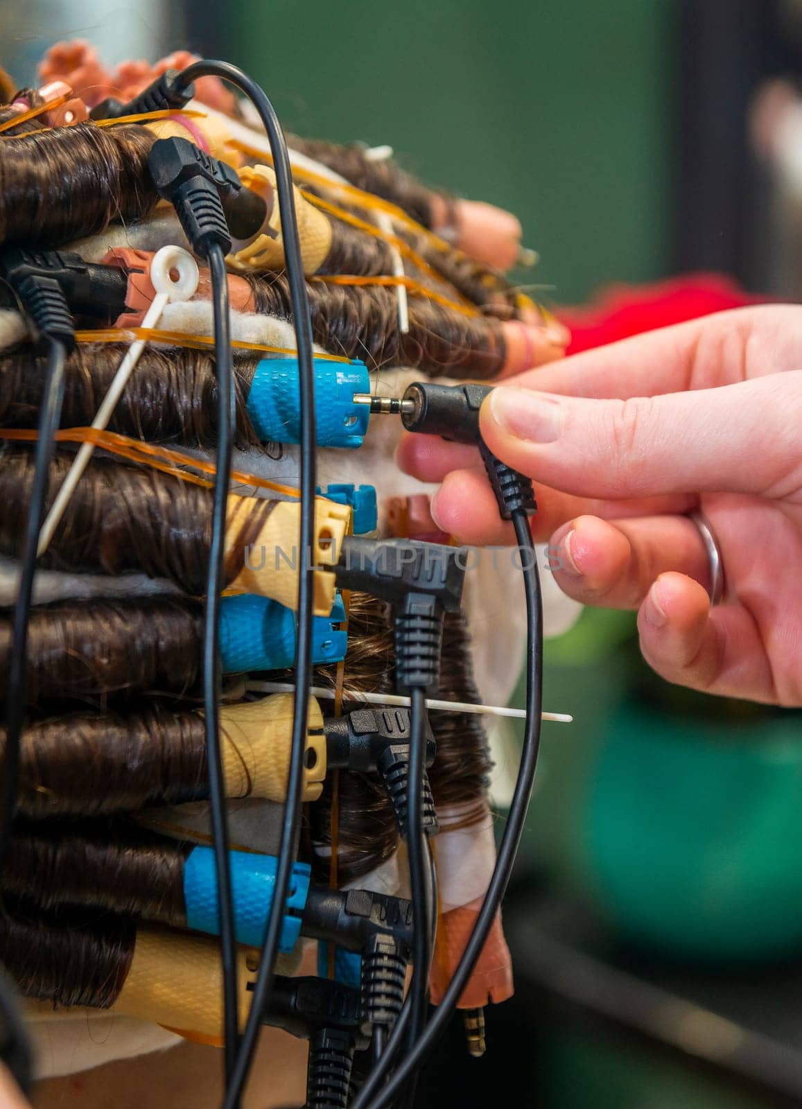 modern process of hair treatment and curling. client sits in chair with curlers on her head. device treats and makes hair curly and wavy. master adjusts curlers, close-up of curlers on client's head