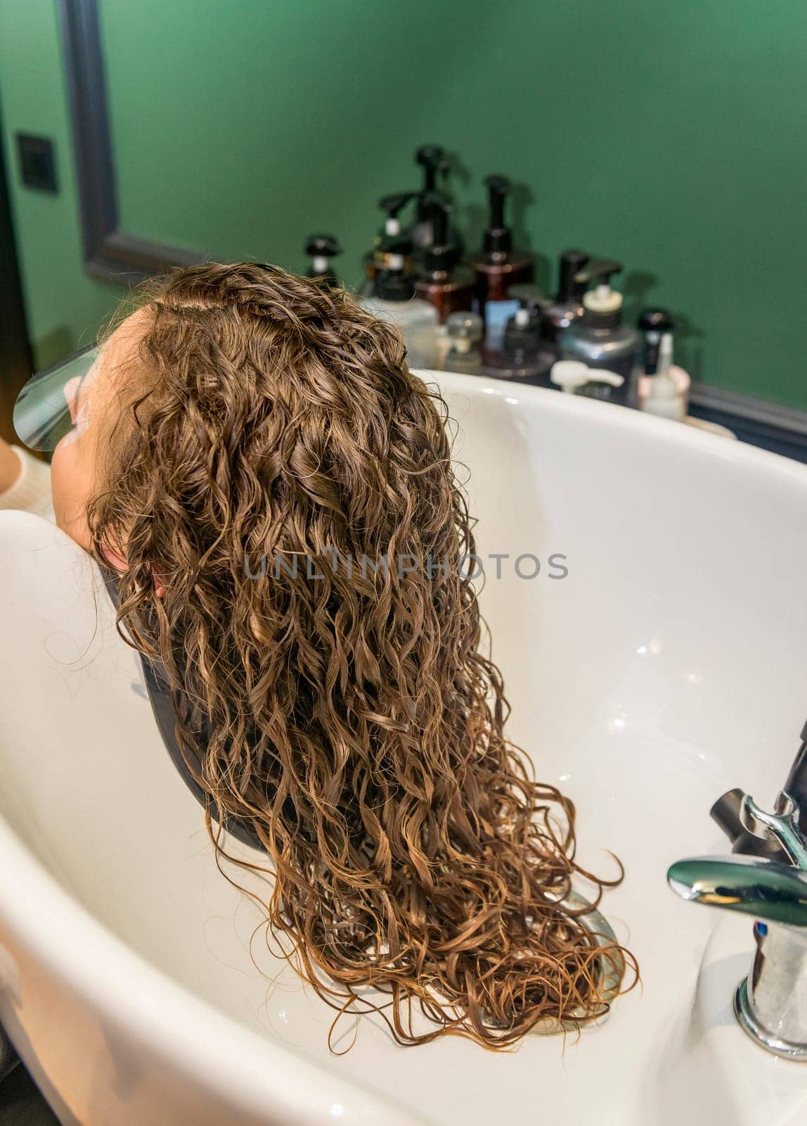 client's hair is washed in a beauty salon. we see a white sink and beautiful curly hair of the client's girl. hair is long and wavy after the procedure of styling and hair treatment
