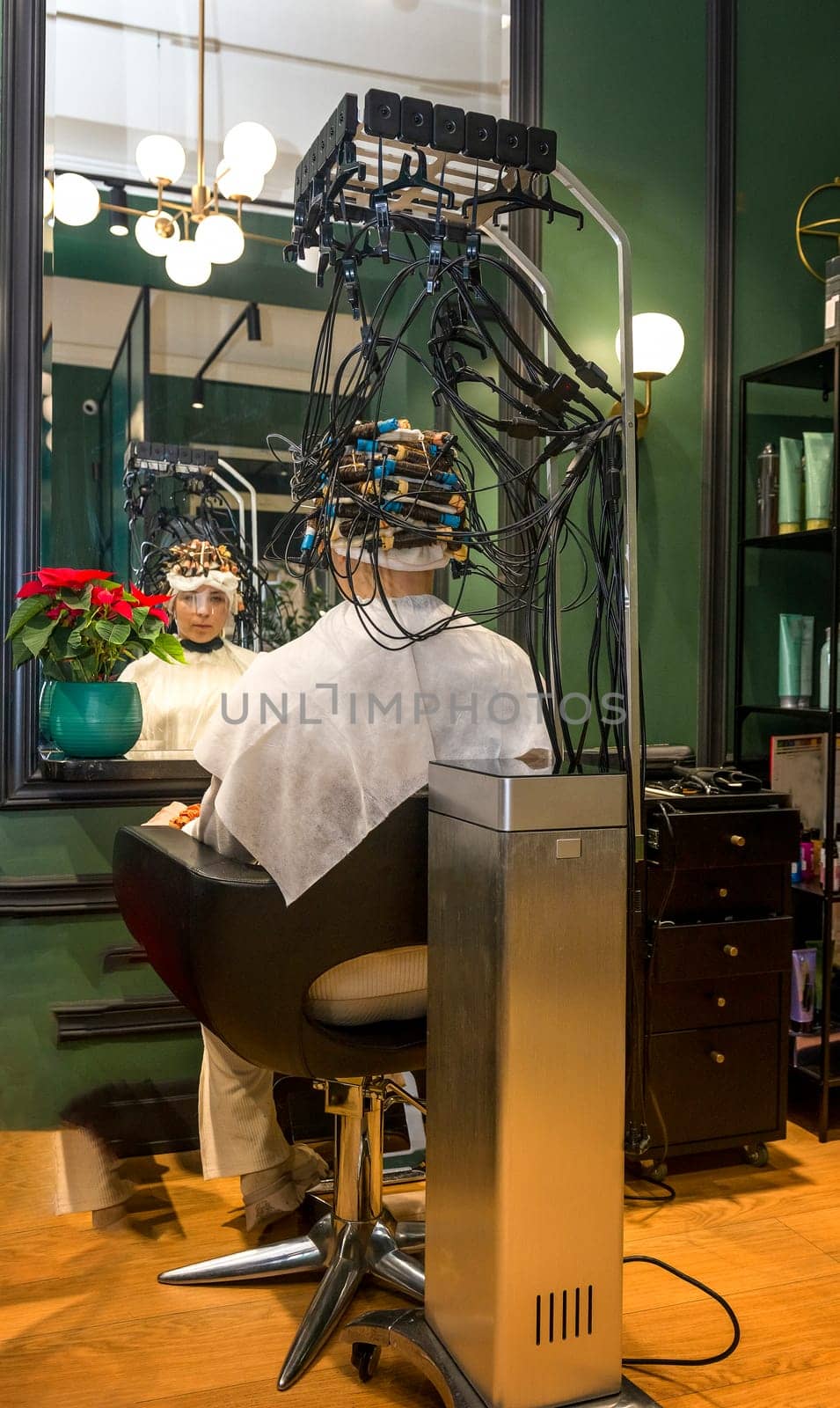 A young girl is getting her hair curled with curlers by a hairdresser. The client is sitting in a chair and her hair is curled with curlers.