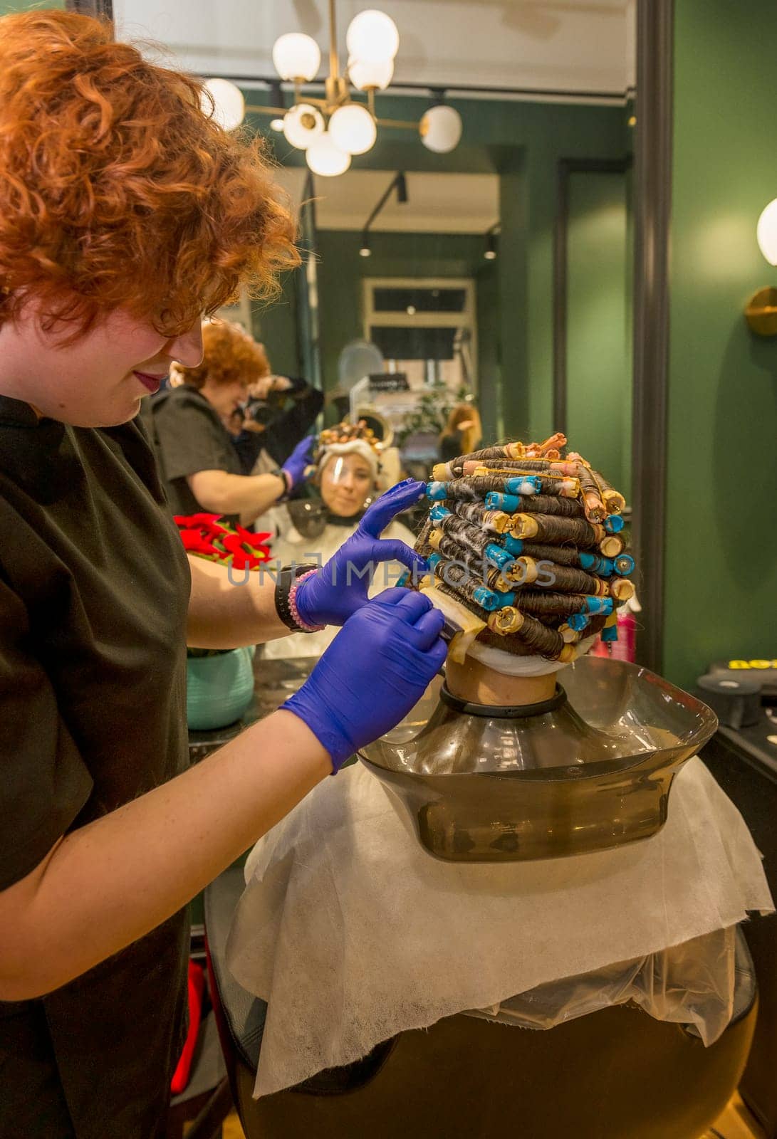 a young girl is getting her hair curled with curlers. the client is sitting in a chair and her hair is curled with curlers. the hairdresser is treating the hair and doing the curling