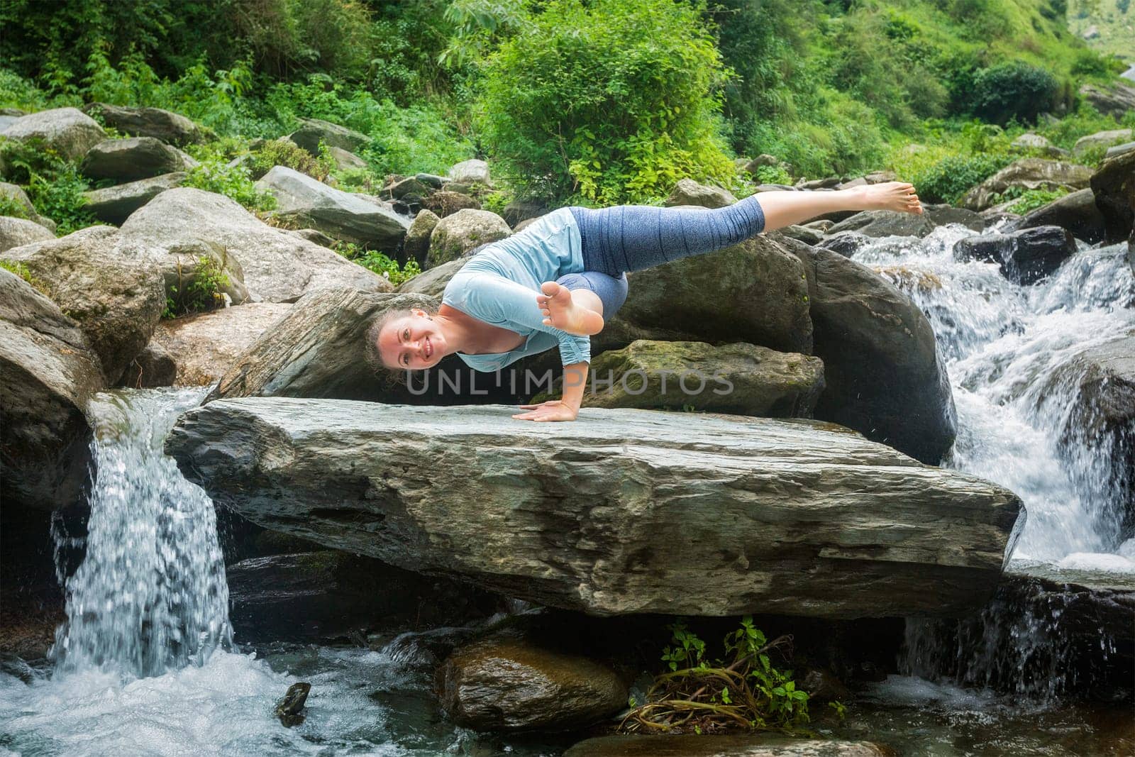 Young fit woman doing yoga oudoors at waterfall by dimol