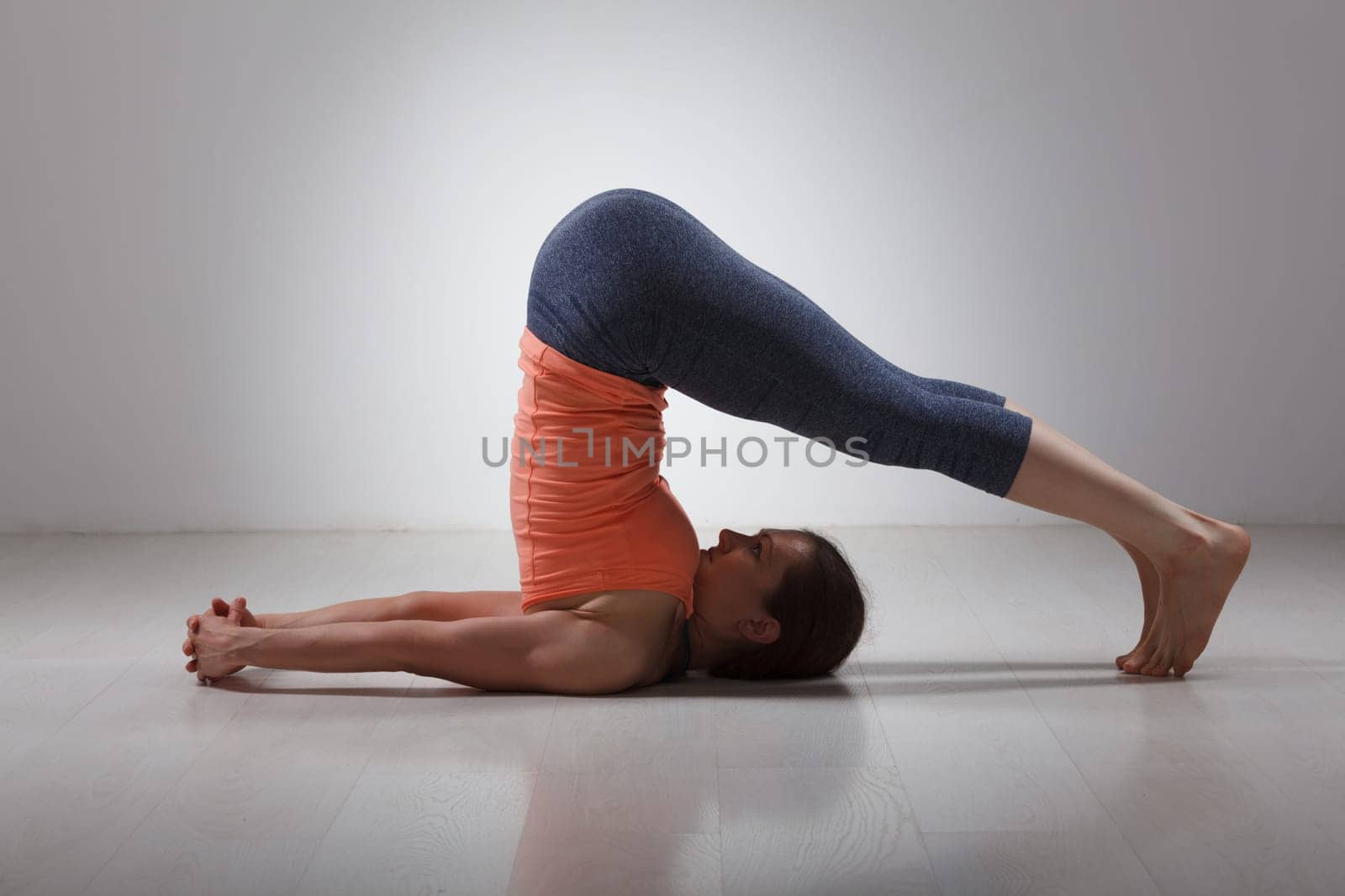 Beautiful sporty fit yogini woman practices yoga asana Halasana - plow pose