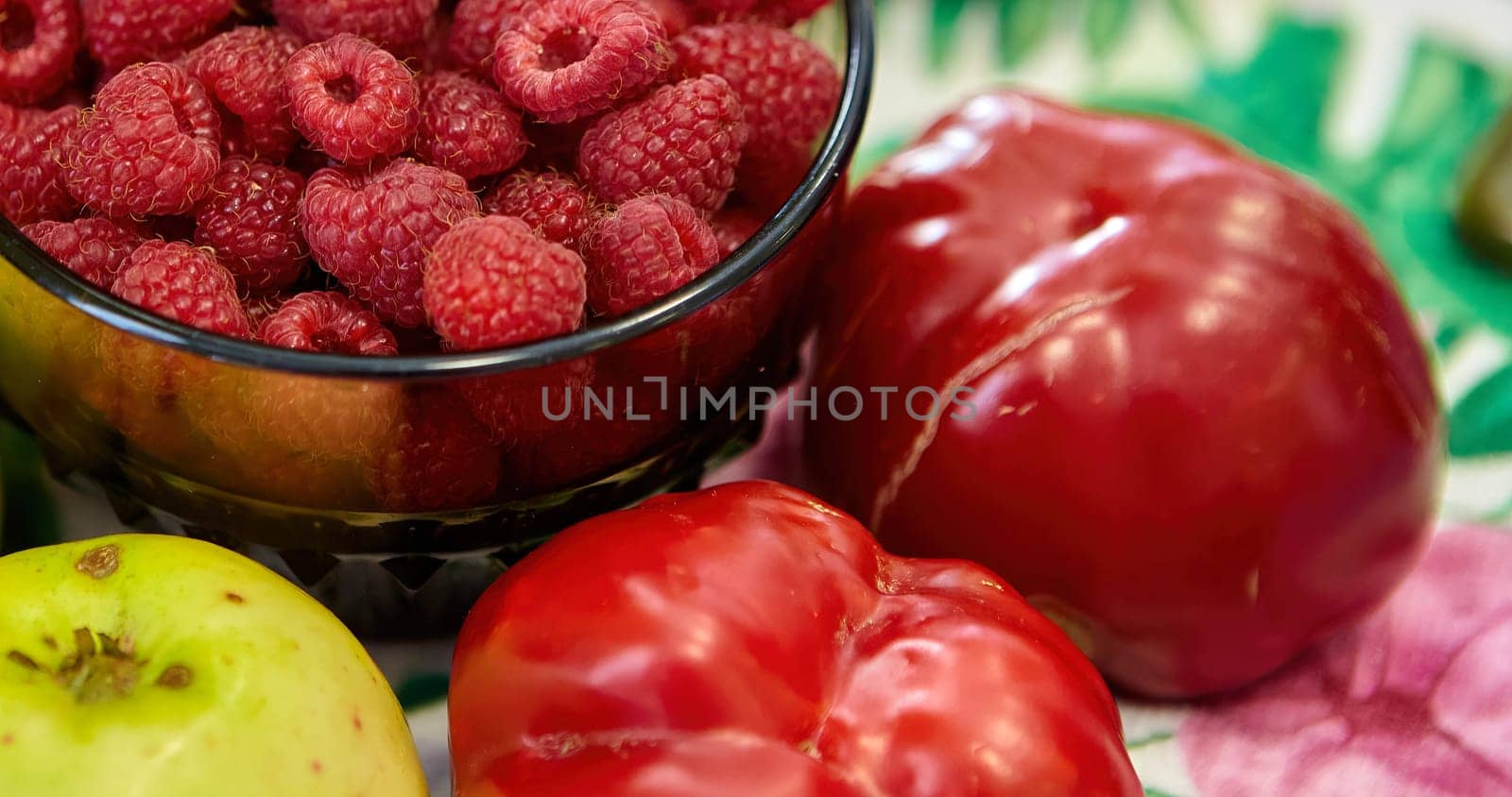 Variety of fresh raw organic fruits and vegetables. Raspberries, apples with tomatoes and red peppers on the table.