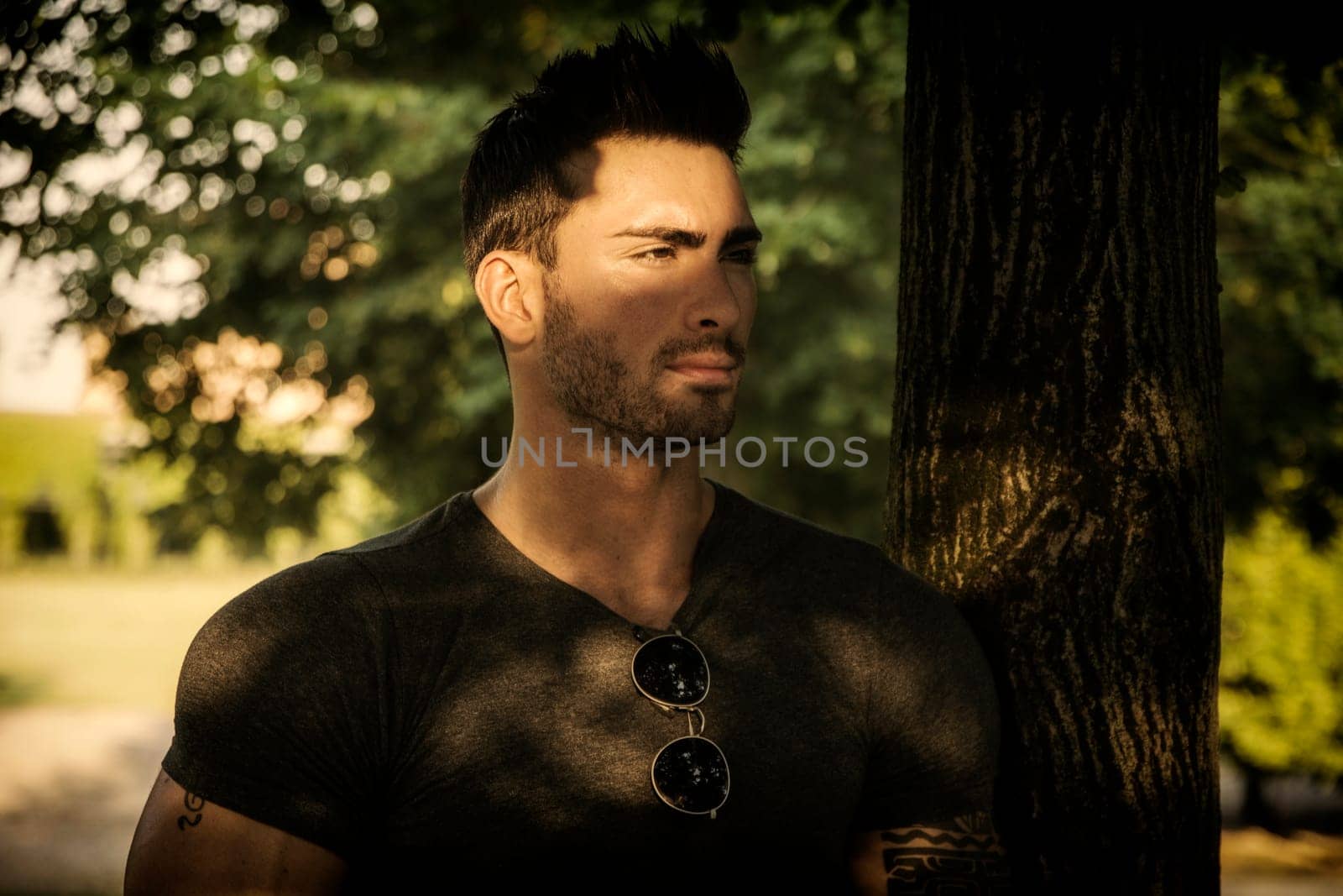 A man standing next to a tree in a park. Photo of a man standing next to a tree in a park