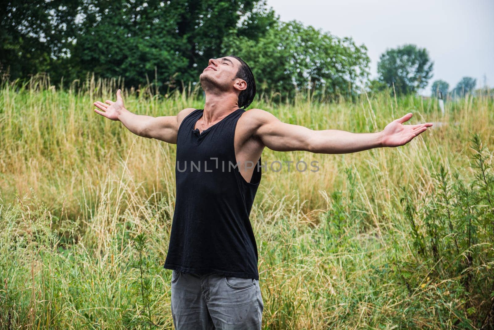 A man standing in a field with his arms outstretched. Photo of a man standing in a field with his arms outstretched in a freedom or liberation concept