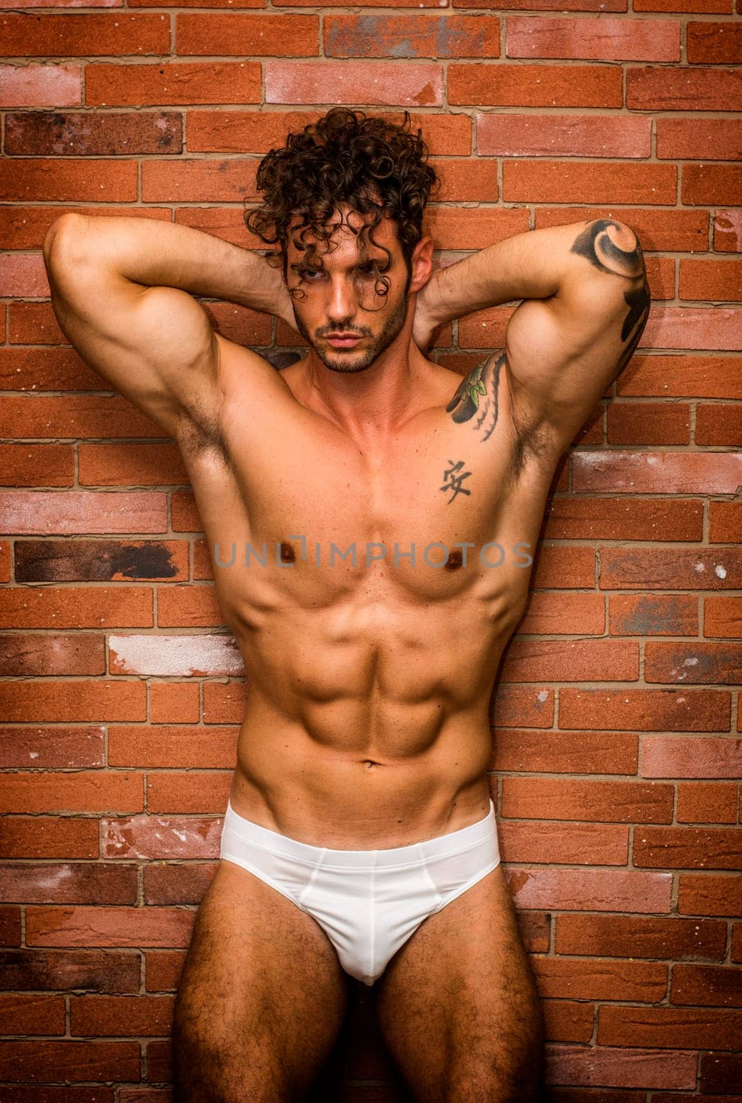 A man in a white underwear posing for a picture. Photo of a confident man in white underwear striking a pose for a photoshoot in front of a brick wall