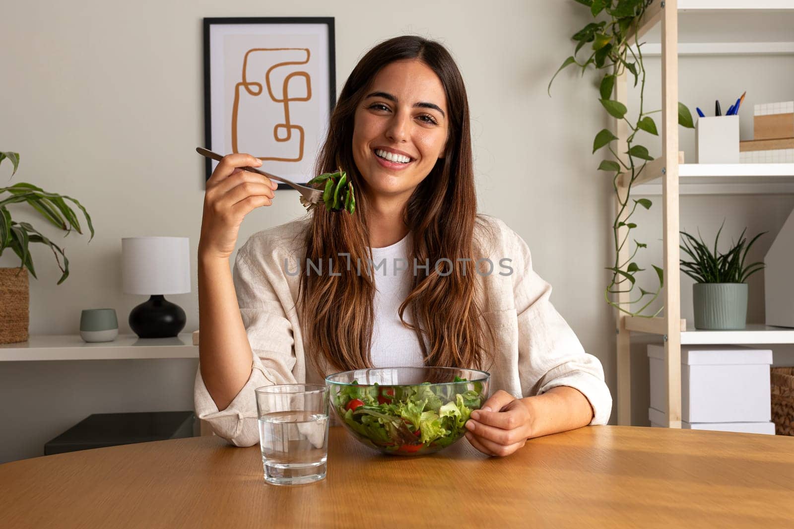 Happy young caucasian woman eating healthy salad at home looking at camera. Healthy lifestyle concept.
