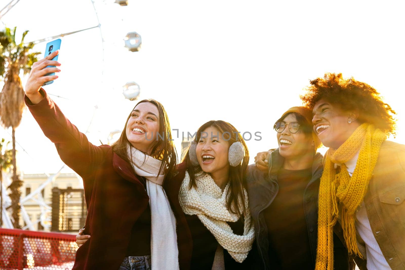 Happy multiracial group of smiling and cheerful college friends taking selfie together in a sunny winter day in the city using mobile phone. Technology and lifestyle concept.