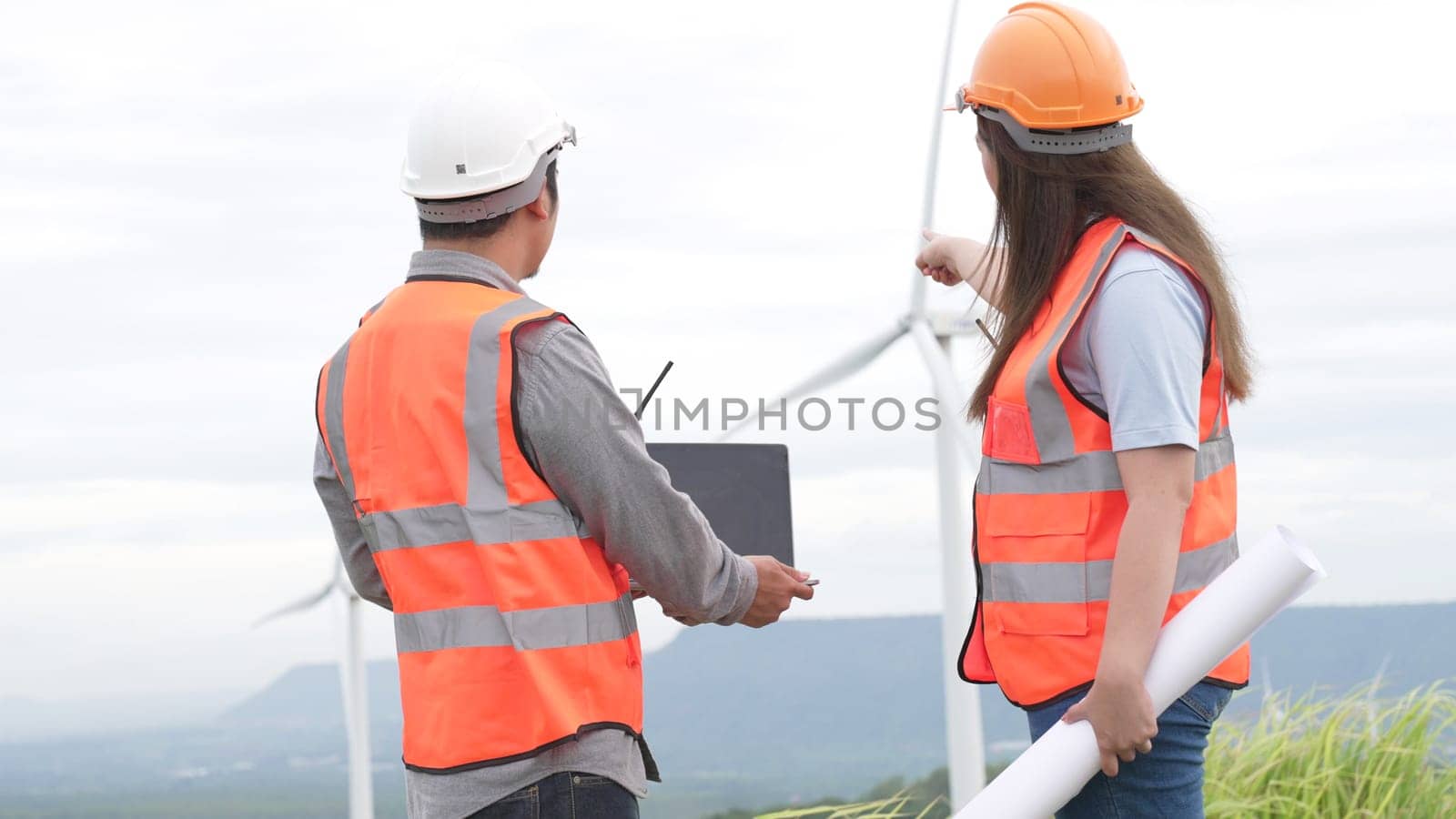 Male and female engineers working on a wind farm atop a hill or mountain in the rural. Progressive ideal for the future production of renewable, sustainable energy.