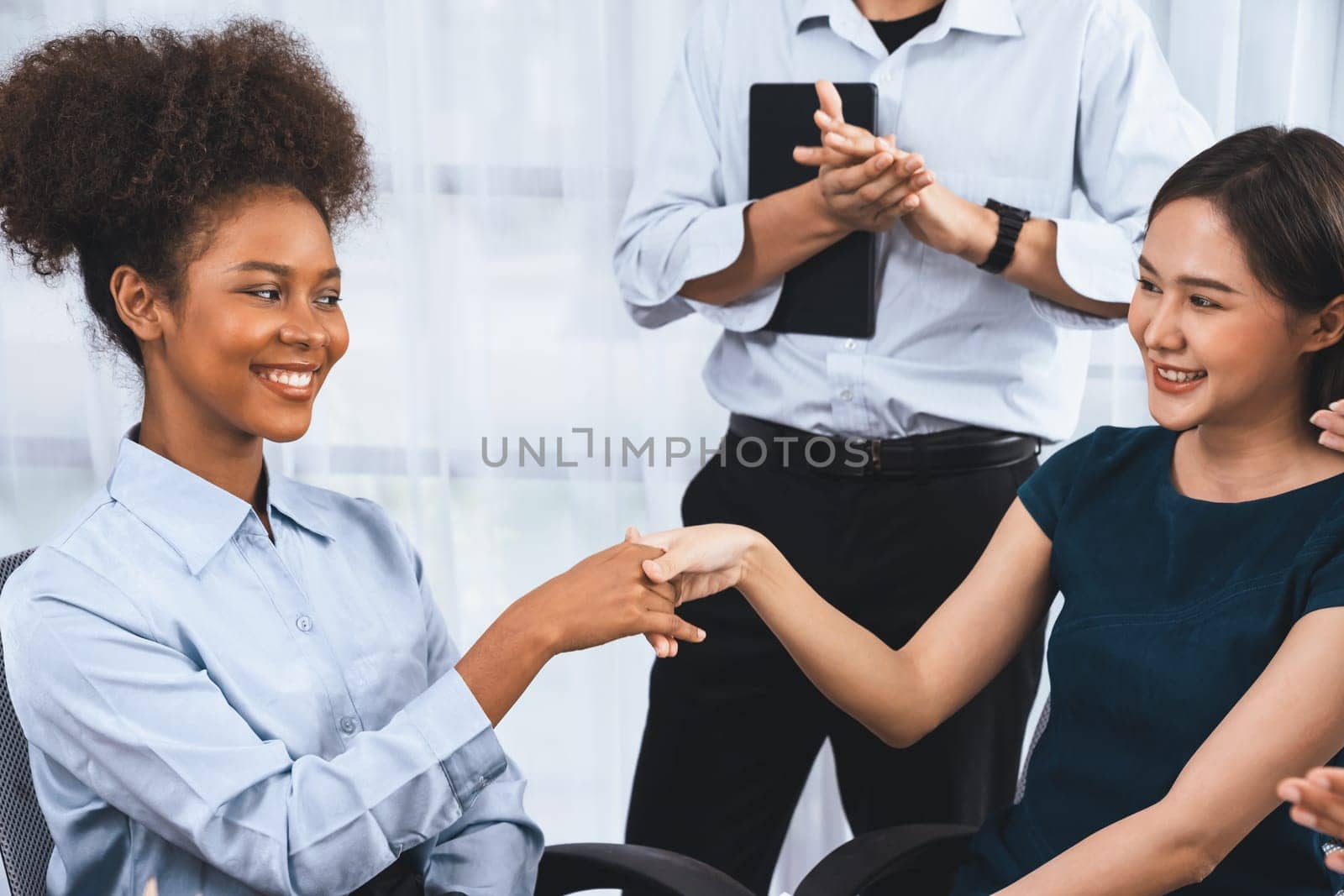 Diverse coworkers celebrate success with handshake and teamwork in corporate workplace. Multicultural team of happy professionals united in solidarity by handshaking in office. Concord