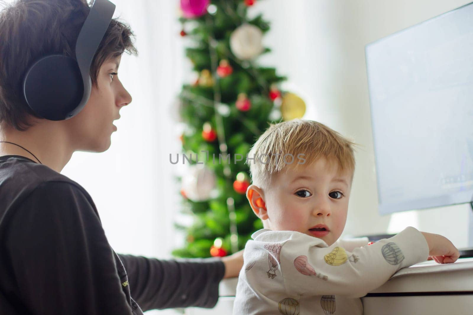 A teenager in headphones holding a baby sitting in front of a computer, the child laughs. High quality photo
