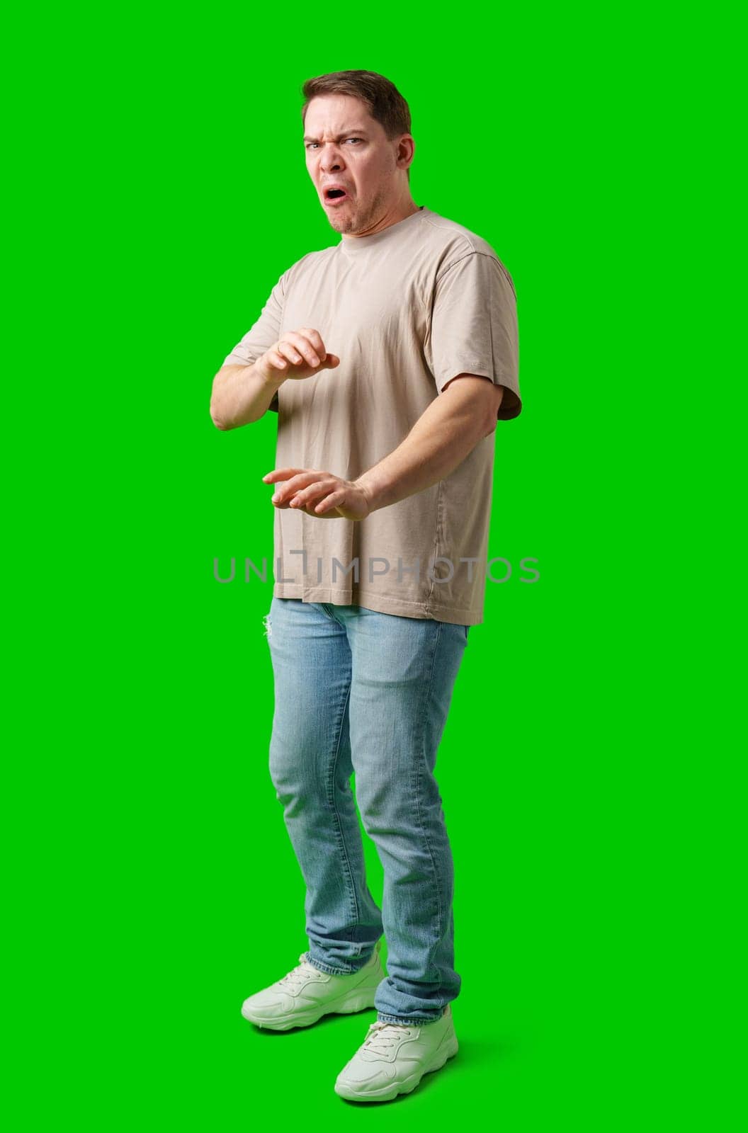 Young man making a disgusted expression while standing against a bright green background in studio