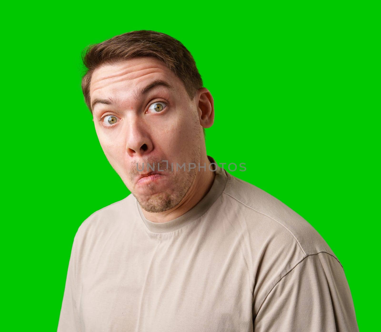A surprised man stands in front of a bright green screen, expressing shock with his mouth open in studio