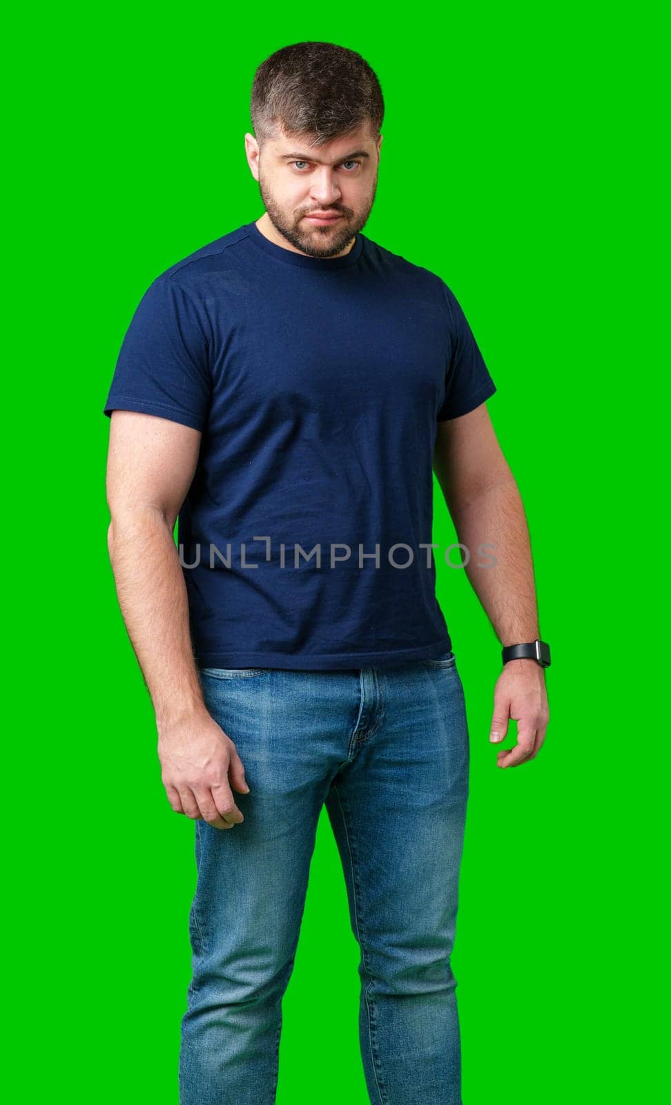 A man stands confidently on a bright green background wearing a dark t-shirt and jeans close up