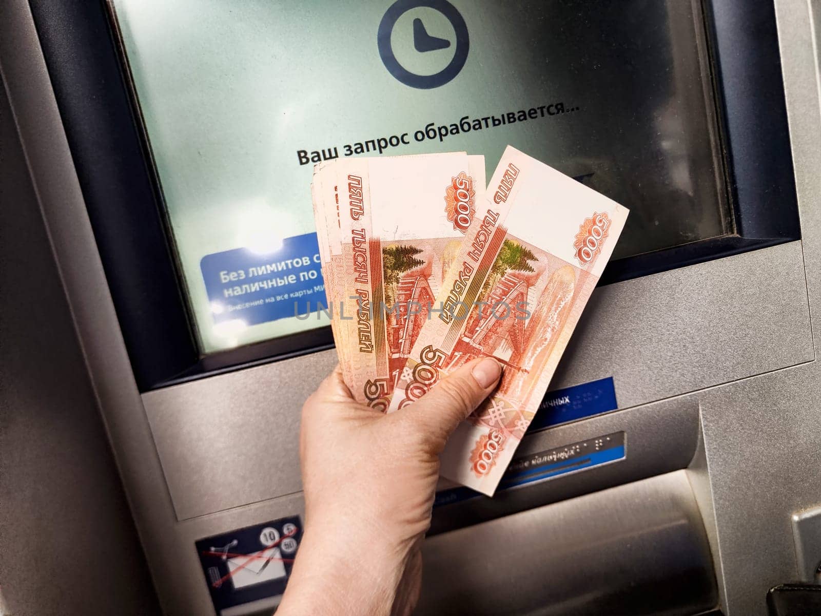 Kirov, Russia - October 08, 2024: A person at an urban ATM is withdrawing cash, displaying several banknotes while waiting for the transaction.