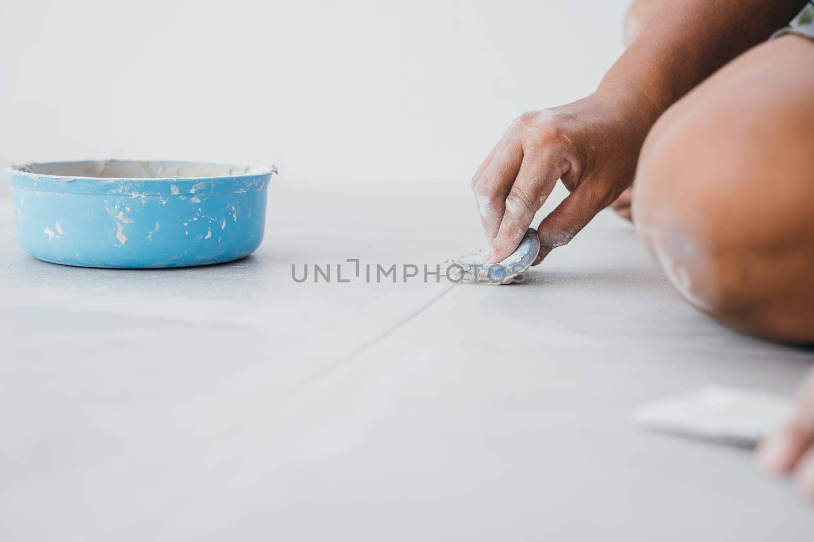 Grouting tiles with a rubber trowel, a hand spreads paste between ceramic tiles on the floor. Tile finishing details in close focus.