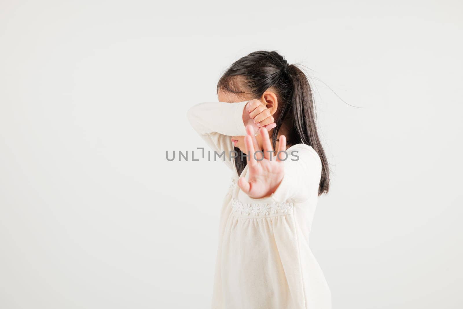 Asian portrait cute young kid girl smiling doing show stop sign gesture with palm of hand but unhappy face studio shot isolated on white background, kindergarten children doubt with copy space
