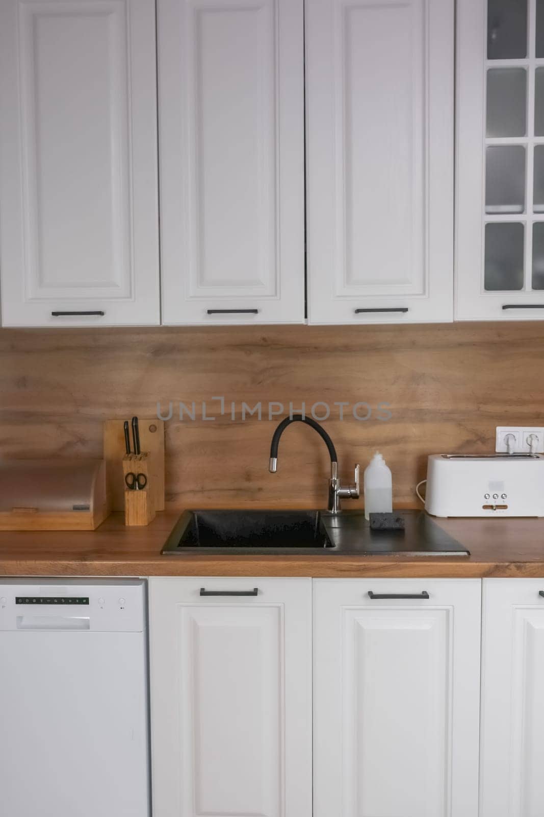 Horizontal photo of a modern kitchen in white and wooden style, in the center is a black kitchen sink, on a wooden countertop there are white wooden appliances for storing and preparing food. Modern kitchen concept, kitchen island, modern kitchen style. High quality photo